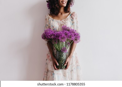 Laughing winsome girl with brown skin holding vase of alliums. Indoor portrait of attractive african woman posing with purple flowers. - Powered by Shutterstock