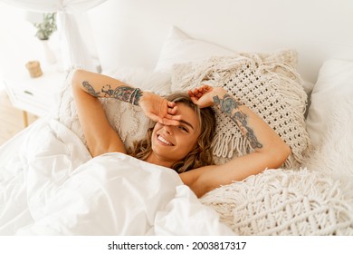 Laughing woman chilling in her bed. Tatoo on hends. Cozy home lifestyle. 