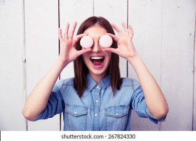 Laughing woman closing her eyes with round cookies with wooden wall on background