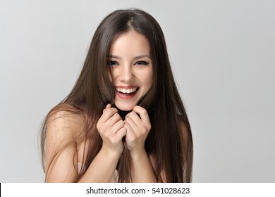Laughing woman covers her face with long hair. Beautiful woman with bare shoulders has a clean well-groomed skin and long straight hair. Close-up portrait against a light gray background.