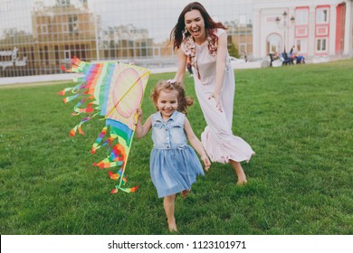 Laughing Woman In Light Dress And Little Cute Child Baby Girl Running, Catching Up And Play With Colorful Kite In Park. Mother, Little Kid Daughter. Mother's Day, Love Family, Parenthood, Childhood