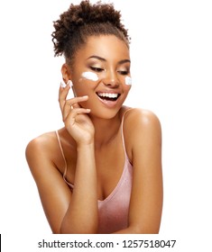 Laughing Woman With Moisturizing Cream On Her Face. Photo Of African American Woman With Flawless Skin On White Background. Skin Care And Beauty Concept