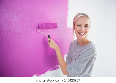 Laughing Woman Painting Her Wall In Pink And Looking At Camera