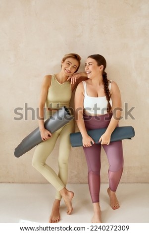 Laughing Women Embracing After Yoga. Female Friends Laughing And Holding Yoga Mats After Yoga Session Together At Home. Attractive Girls In Sportswear Spending Free Leisure Time