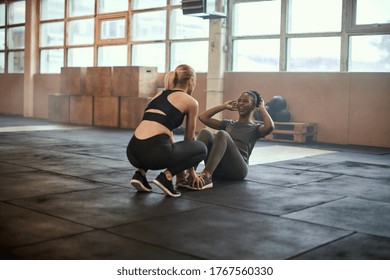 Laughing Young African American Woman Doing Sit-ups With A Workout Partner On The Floor Of A Gym