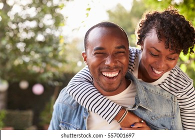 Laughing young black couple piggyback in garden, to camera - Powered by Shutterstock