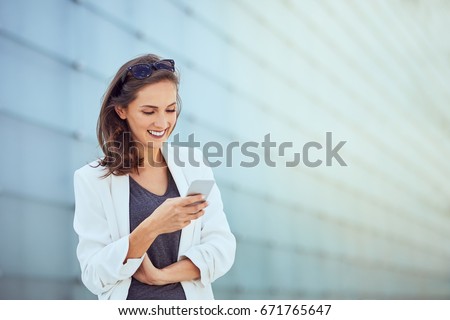 Laughing young businesswoman texting coworker in bright modern outside setting