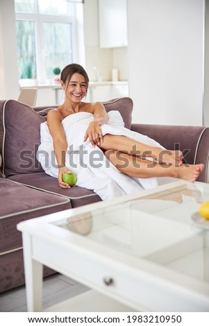 Laughing young Caucasian female with apple in hand resting in home apartment