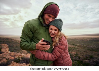 Laughing young couple embracing during camp on mountains looking at smartphone in winter clothing - Powered by Shutterstock