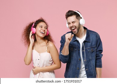 Laughing Young Couple Two Friends European Guy African American Girl In Casual Clothes Isolated On Pastel Pink Background In Studio. People Lifestyle Concept. Listen Music With Headphones, Sing Song