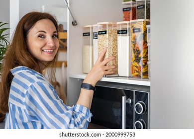 Laughing young female housewife posing during general cleaning, tidying up in cupboard kitchen. Woman placing, sorting food into pp boxes for comfortable storage at cuisine having positive emotion