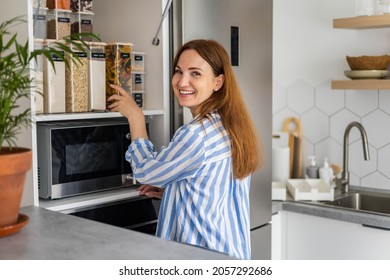 Laughing Young Female Housewife Posing During General Cleaning, Tidying Up In Cupboard Kitchen. Woman Placing, Sorting Food Into Pp Boxes For Comfortable Storage At Cuisine Having Positive Emotion