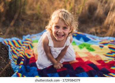 Laughing Young Girl Sitting On Bold Quilt Among Neutral Nature Colors