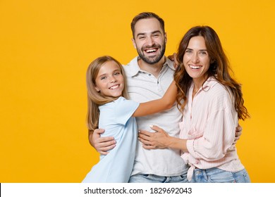 Laughing Young Happy Parents Mom Dad With Child Kid Daughter Teen Girl In Basic T-shirts Hugging Looking Camera Isolated On Yellow Background Studio Portrait. Family Day Parenthood Childhood Concept