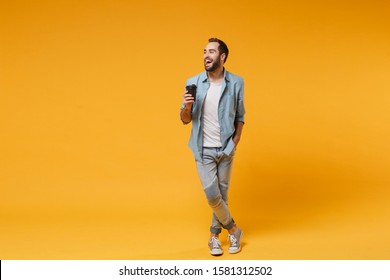 Laughing young man in casual blue shirt posing isolated on yellow orange background, studio portrait. People emotions lifestyle concept. Mock up copy space. Hold cup of coffee or tea, looking aside - Powered by Shutterstock