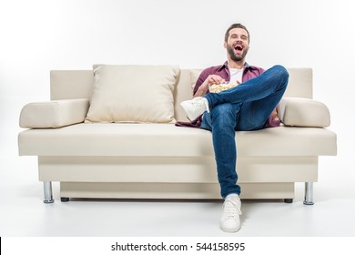 Laughing Young Man Sitting On Couch With Popcorn Isolated On White