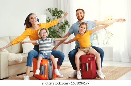 Laughing Young Man And Woman With Children Sitting On Suitcases At Home Holding Hands Apart In Flight Ready For Summer Vacation
