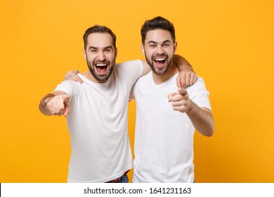 Laughing young men guys friends in white blank empty t-shirts posing isolated on yellow orange background studio portrait. People lifestyle concept. Mock up copy space. Point index fingers on camera - Shutterstock ID 1641231163