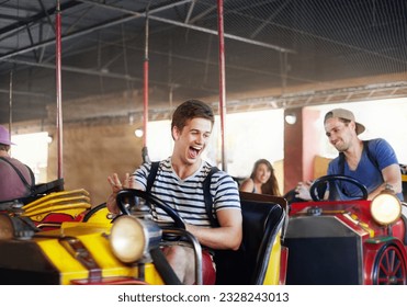 Laughing young men riding bumper cars at amusement park