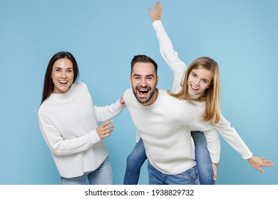 Laughing Young Parents Mom Dad With Child Kid Daughter Teen Girl In White Sweaters Giving Piggyback Ride To Joyful Sitting On Back Isolated On Blue Background. Family Day Parenthood Childhood Concept