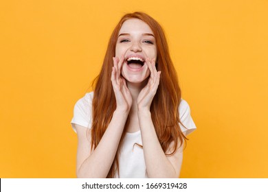 Laughing young redhead woman girl in white blank empty t-shirt posing isolated on yellow background studio portrait. People lifestyle concept. Mock up copy space. Scream with hans gesture near mouth