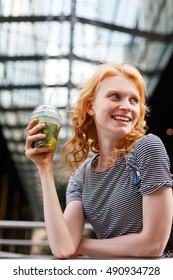 Laughing young redhead woman holding fresh mojito in hand outdoor