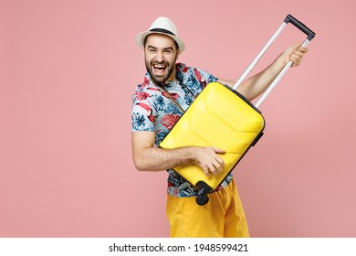 Laughing young traveler tourist man in summer clothes hat hold suitcase like playing guitar isolated on pink background studio portrait. Passenger traveling on weekends. Air flight journey concept - Shutterstock ID 1948599421