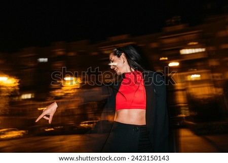 Laughing young woman with dark hair enjoys a vibrant night scene with dynamic light painting effects, pointing playfully.