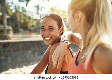 Laughing Young Woman In Sportswear Sitting With Her Workout Partner Outside On A Sunny Day