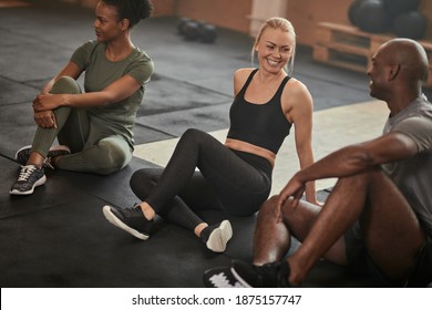 Laughing young woman talking with a group of diverse young friends while sitting on a gym floor after a workout - Powered by Shutterstock