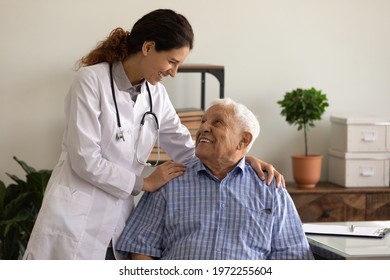 Laughter is the best medicine. Optimistic young lady doc embrace shoulders of laughing old man sitting on chair at clinic office. Doctor joking with aged patient give support motivation on good result - Shutterstock ID 1972255604