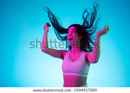 Laughting, dancing with hair blowed out. Brunette woman's portrait on blue studio background in mixed neon. Beautiful model in white top. Concept of human emotions, facial expression, sales, ad Stock photo © 