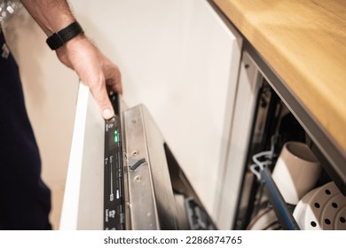 Launching a washing machine filled with dirty dishes in the kitchen close-up of an unrecognizable man. Man pressing button of dishwasher. Selective focus