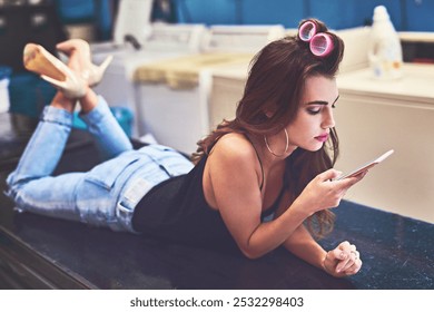 Laundromat, relax and woman with smartphone, routine and washing machine for chores, cool and cleaning. Fashion, waiting and person in laundry room, responsibilities and communication with contact - Powered by Shutterstock