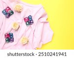 Laundry detergent pods, t-shirt and flowers on yellow background, flat lay. Space for text