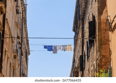 Laundry drying on clothesline between Venetian buildings. Colorful laundry hangs on a clothesline stretched between two old buildings in Venice, Italy, under a clear blue sky.