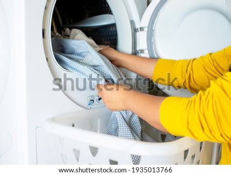 Laundry at home. Cropped view of young housewife take dried clean colors clothes out of the tumble dryer machine. Concept of modern household equipment and technology for modern lifestyle. 