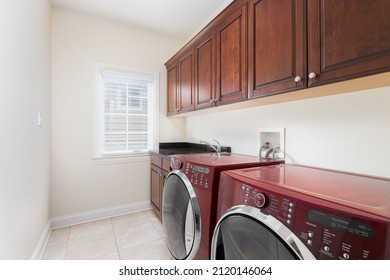 A Laundry Room With Red Washer And Dryer Appliances And Dark Hardwood Cabinets.