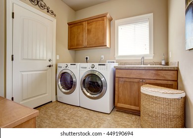 Laundry Room With Washer And Dryer. Wooden Cabinets And Tile Floor