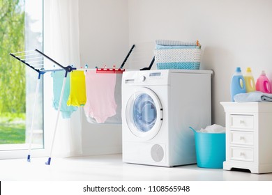 Laundry room with washing machine or tumble dryer. Modern household devices in white sunny home. Clean washed clothes on drying rack. Liquid washing detergent in plastic bottle and fabric softener.