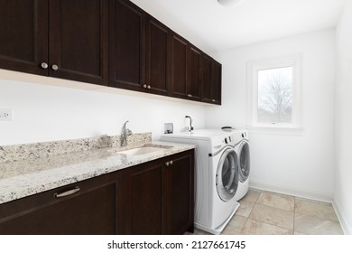 A Laundry Room With White Washer And Dryer Appliances, Dark Mahogany Wood Cabinets, And Granite Countertop.