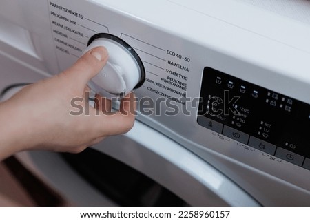 Laundry Setting Washing Machine Dial to ECO Mode for Energy Saving and Environmental Conservation in Bathroom. Close Up Shooting with a Hand Rotating the Front Panel Button the Laundry Machine.
