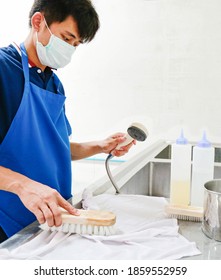 A Laundry Staff Is Holding A Shower Head, Brushing A Napkin In Process Of Stain Removal Spotting Chemicals. Shot Taken In The Factory.