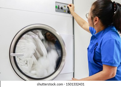 A Laundry Staff Wearing A Dark Blue Polo Shirt Is Turning Heat Temperature Of Industrial Dryer Machine. Shot Taken In The Factory.