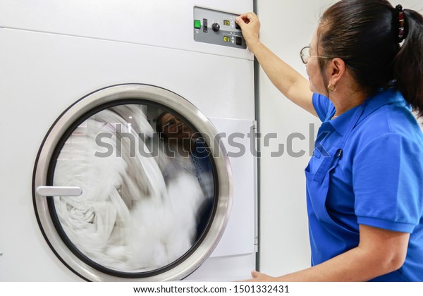 A laundry staff wearing a dark blue polo shirt\
is turning heat temperature of Industrial dryer machine. Shot taken\
in the factory.