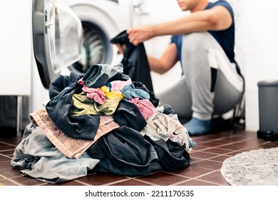 Laundry, washing clothes. Man loading washer machine and sorting by color and fabric.  Male homemaker doing house chores. Domestic work in family. Young dad and parent putting clothing in dryer. - Shutterstock ID 2211170535