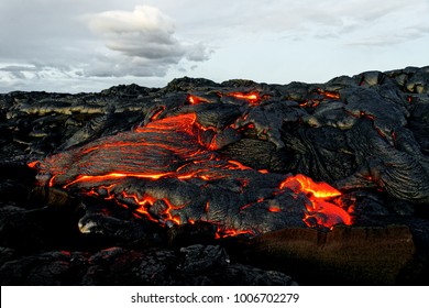 A lava flow emerges from a rock column and pours into a black volcanic landscape, in the background the first daylight - Location: Hawaii, Big Island, volcano "Kilauea"                      