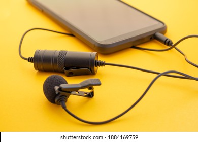 Lavalier Or Lapel Microphone On A Colored Surface Plugged Into A Cell Phone. Details Of The Grip Clip Or Fastener, Mic Power Bank, Miniplug, And Wind Sponge Are Visible. Concept Useful Object