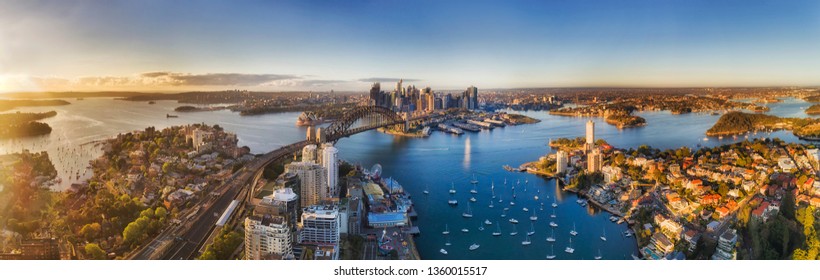 Lavender bay from lower North Shore on Sydney harbour agains major city CBD landmarks around the Sydney Harbour bridge in soft warm morning light seen from mid-air over roof tops.
