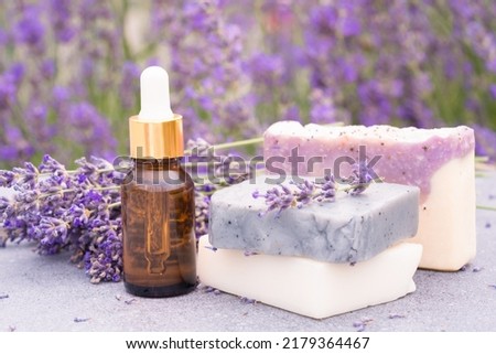 Lavender beauty products - cosmetic oil or face serum and natural handmade soap bars against lavender flowers field as background with copy space. Herbal cosmetics 